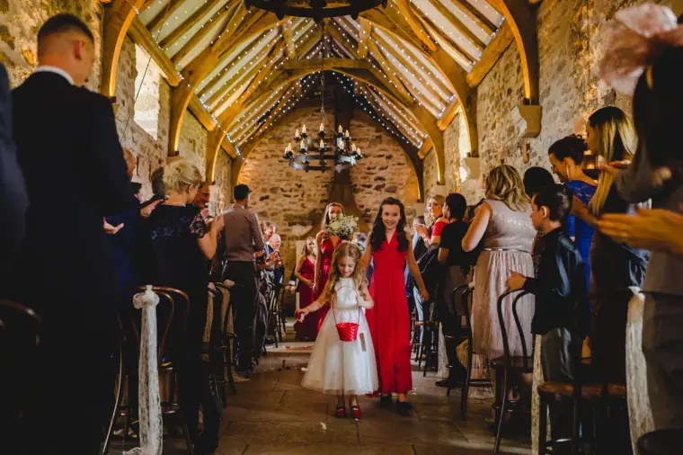Bridesmaid in red and a young bridesmaid walking up the aisle past applauding guests