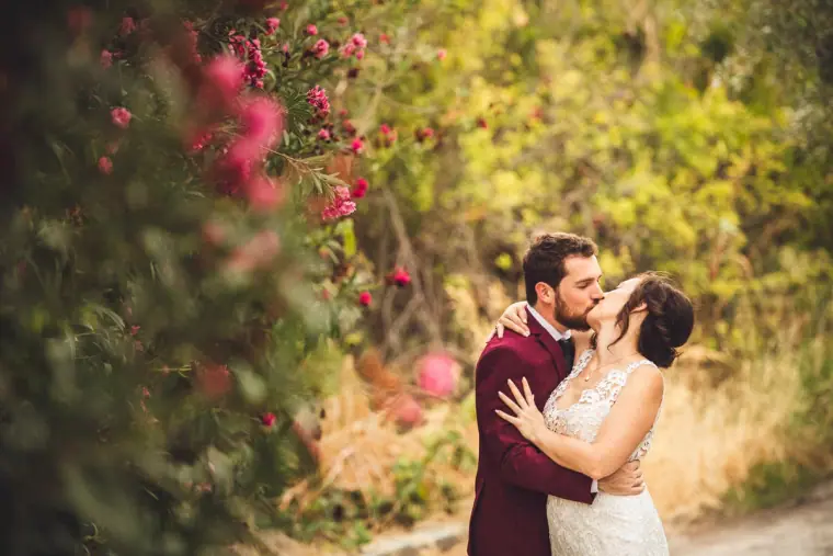 Bride and groom kissing beside pink oleander bushes in warm evening light
