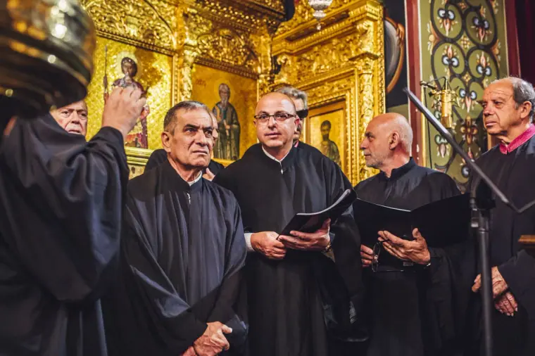 Chanters in black robes singing beside gilded icons inside the church