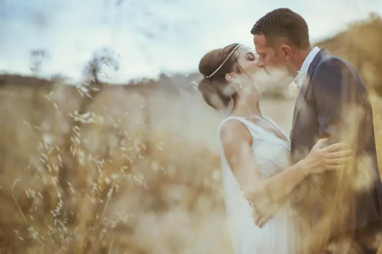 Bride and groom kissing among golden grasses in soft evening light