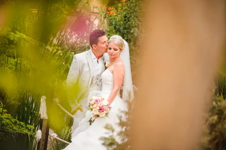 Nathan kissing Charlotte's forehead among flowering shrubs
