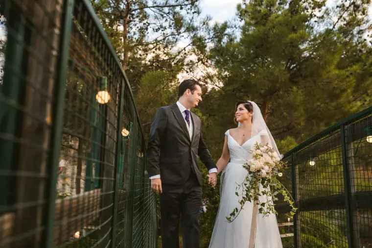 Couple holding hands on the green footbridge, the bride holding a trailing white bouquet