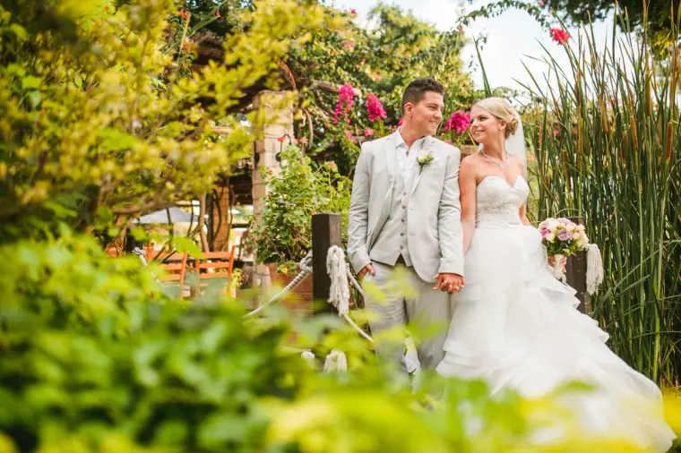 Newlyweds standing on a garden walkway surrounded by bougainvillea and greenery