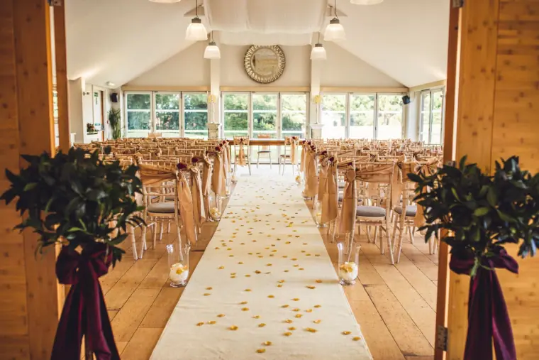 Ceremony room aisle flanked by bay trees with burgundy ribbons at Wasing Park