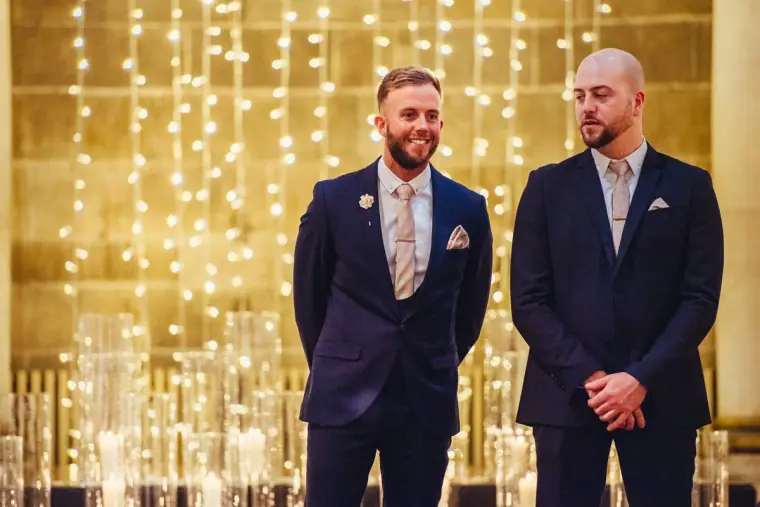 Groom and best man standing in front of a curtain of fairy lights