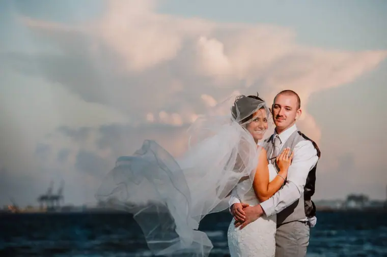 Louise and Mike embracing by the sea under a towering evening cloud
