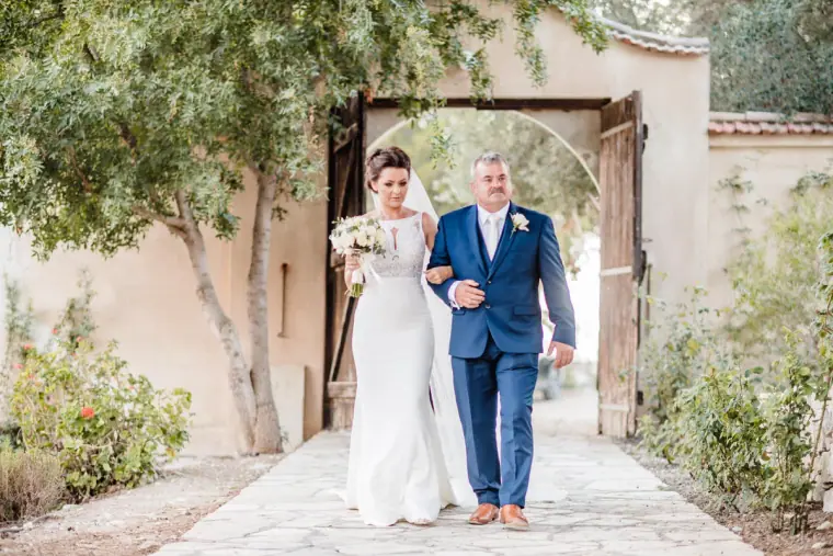 Bride walking through the monastery gates on the arm of a man in a navy suit