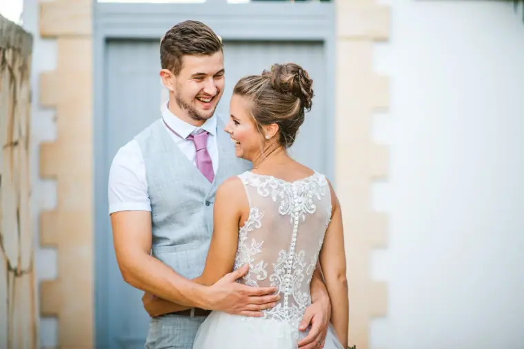 Groom laughing as he holds his bride by a blue wooden gate