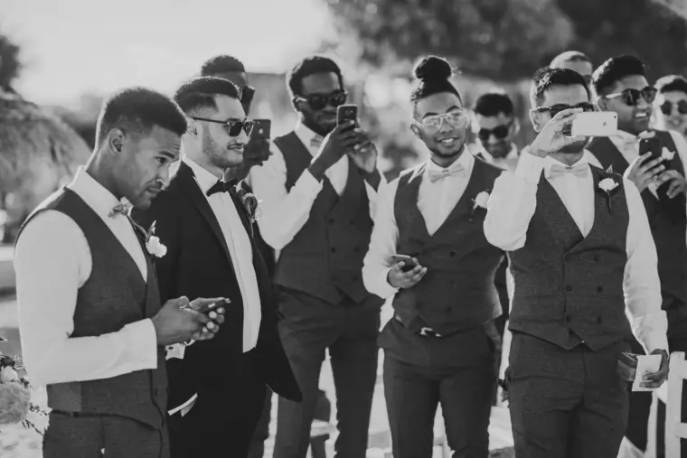 Black-and-white photo of groomsmen filming the bride's arrival on their phones