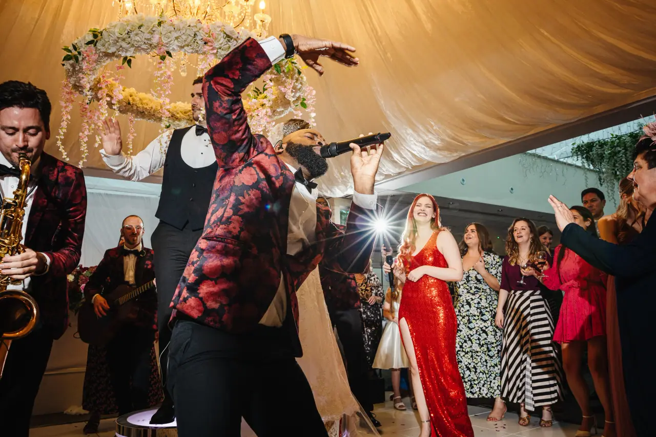 Performer in a red patterned jacket dancing among guests beneath a floral hoop