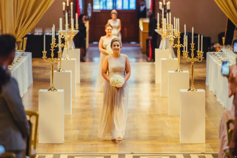 Bridesmaid walking down the aisle between candelabras and white plinths