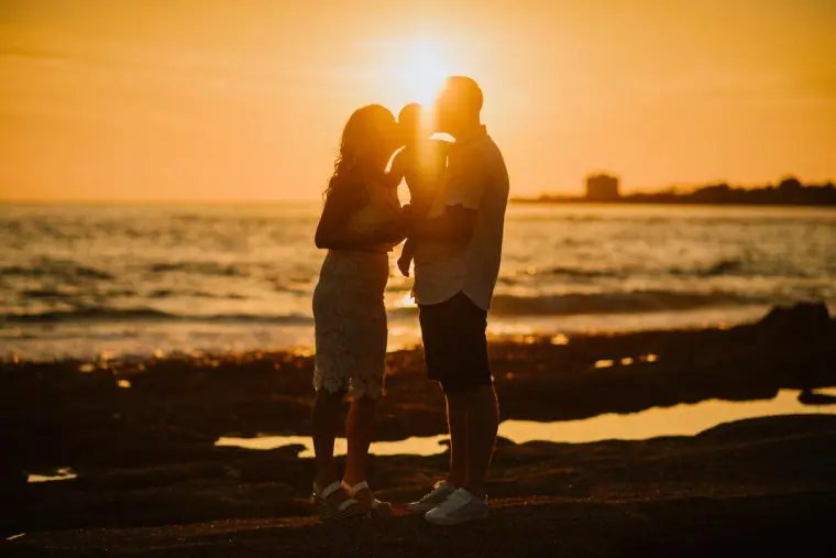 Silhouetted couple embracing on the shore as the sun sets over the sea in Paphos