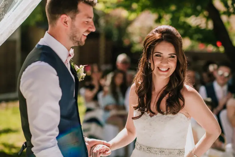 Claire and Sean laughing together at their outdoor ceremony beneath green trees, Vasilias Nikoklis Inn