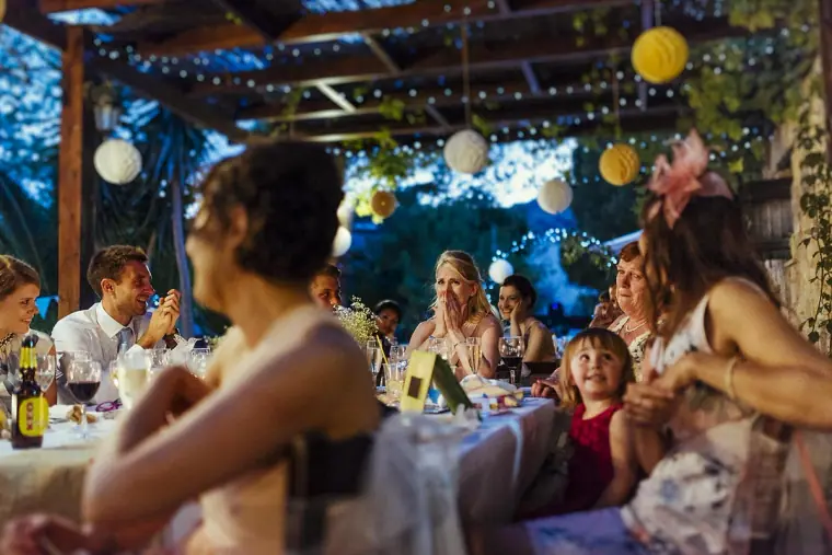Guests listening at long tables beneath lanterns and string lights