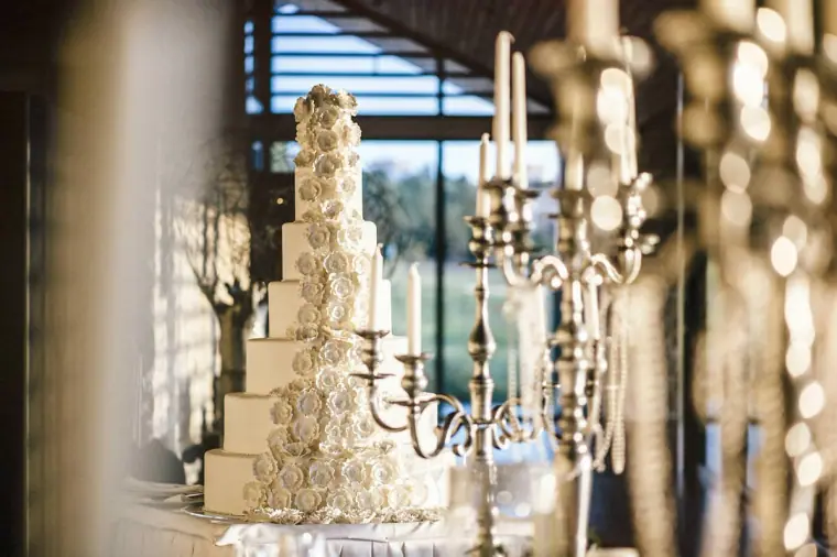 Tall white wedding cake covered in sugar roses beside silver candelabras