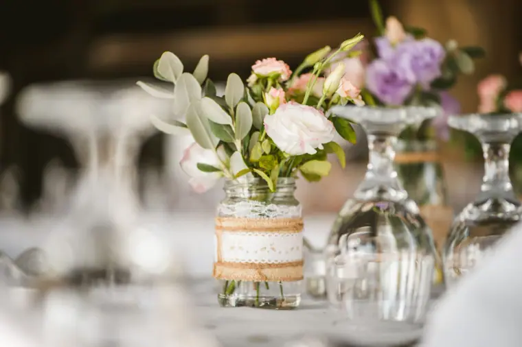 Jar of pastel flowers and wine glasses on a reception table
