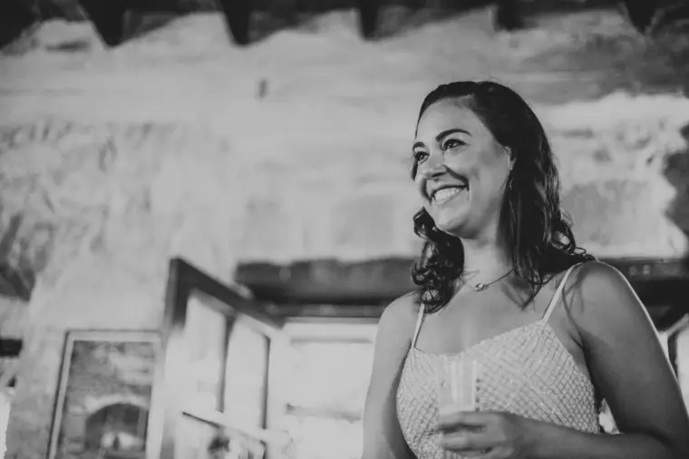 Black-and-white photo of a smiling bridesmaid holding a drink indoors
