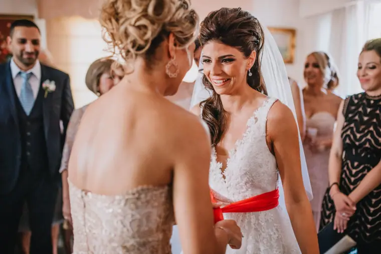 Bride smiling as a red ribbon is tied around her waist, guests watching, Four Seasons Limassol