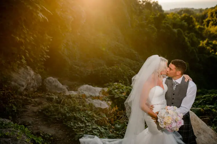 Ben kissing Maryellen among the rocks at golden hour, her bouquet in hand