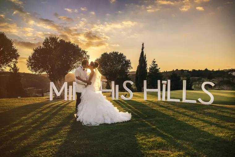 Katie and Paul kissing beside large Minthis Hills letters on the lawn at sunset