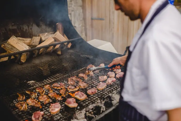 Chef grilling meat over a wood-fired barbecue