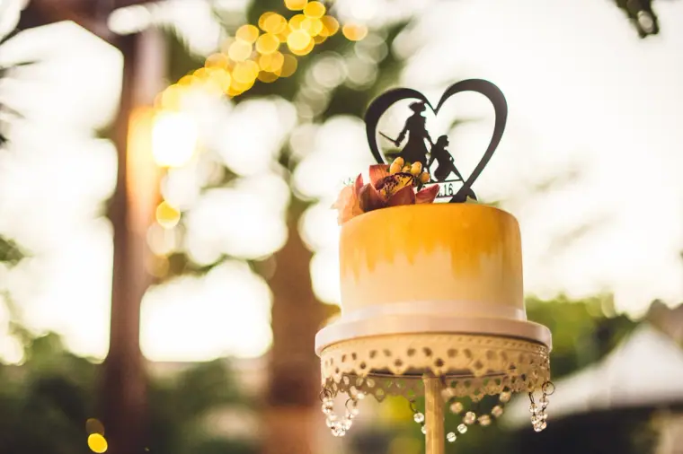 Small golden-yellow wedding cake with a heart-shaped silhouette topper on a lace stand