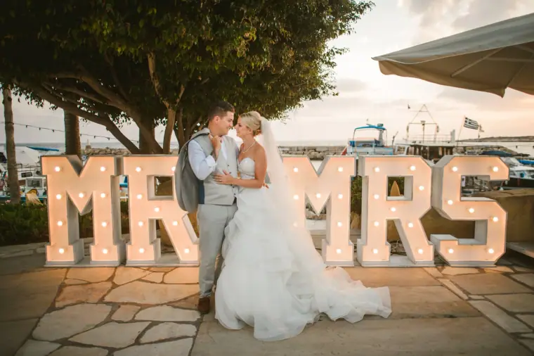Newlyweds kissing behind giant illuminated Mr & Mrs letters