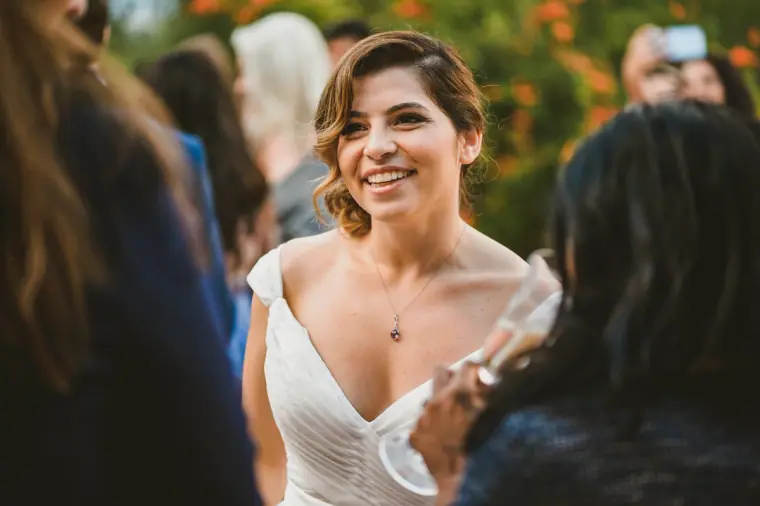 Bride laughing with a glass in hand among guests at the drinks reception