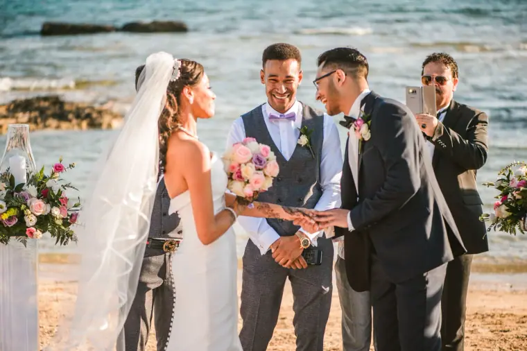 Groom placing the ring on the bride's finger by the sea at Thalassines Beach Villas
