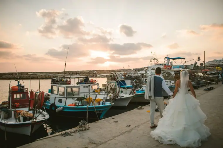 Charlotte and Nathan walking along a harbour lined with fishing boats at sunset