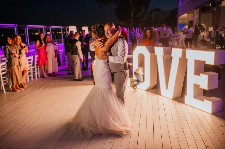 Louise and Mike dancing on the deck beside the glowing LOVE letters as guests watch
