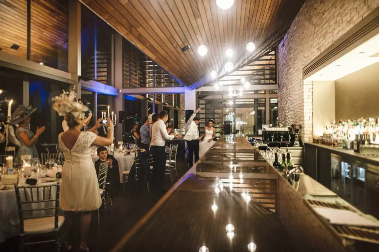 Couple entering the reception hall under a wooden ceiling as guests cheer