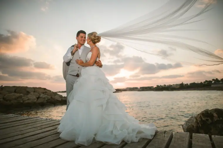 Charlotte's veil blowing in the breeze as the couple embrace on a jetty at sunset