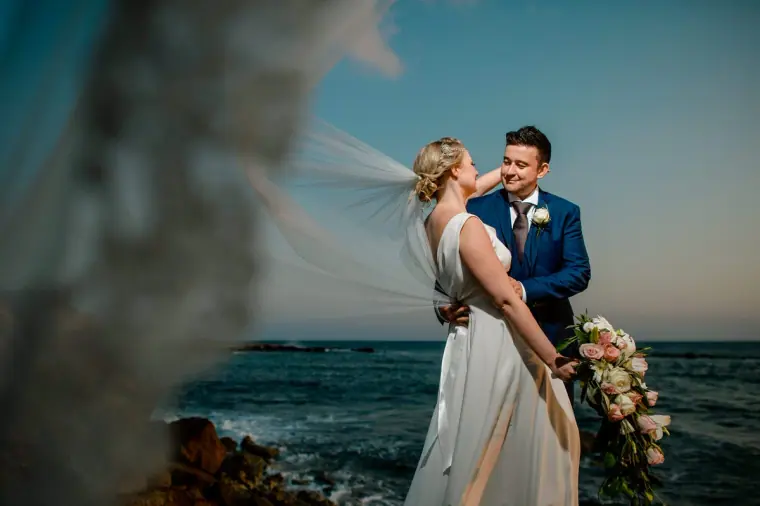 Bride and groom laughing together by the waves with her cascading bouquet