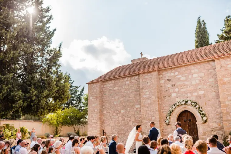 Guests seated before the stone chapel with its floral-garlanded doorway