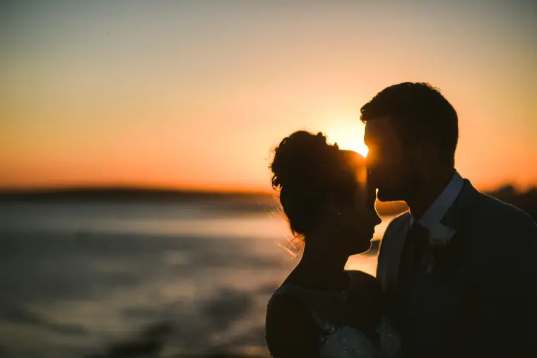 Silhouetted couple touching foreheads against an orange sunset over the sea