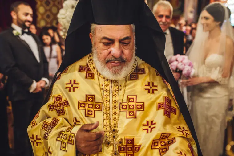Orthodox priest in gold vestments leading the ceremony beside the couple