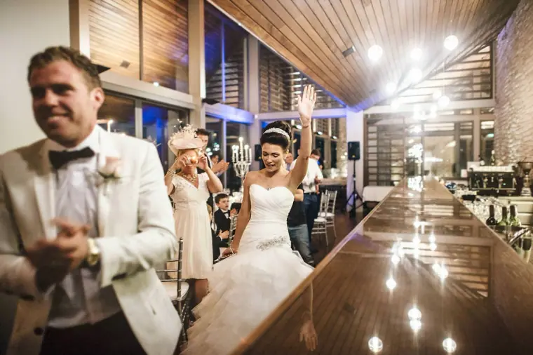 Groom in a white tuxedo jacket and bride waving as they enter the reception