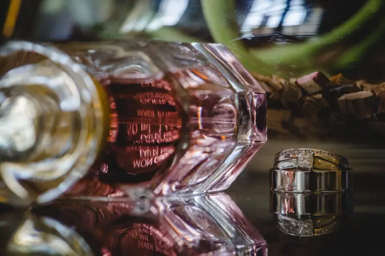 Wedding ring beside a pink perfume bottle on a reflective surface, Aphrodite Hills