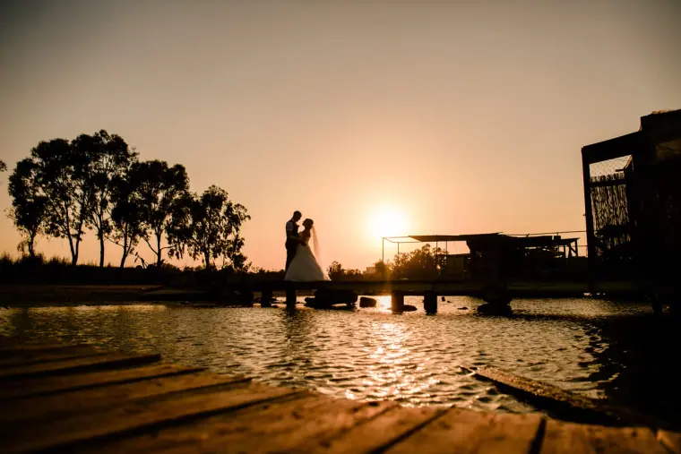 Silhouette of a couple on a jetty by the water as the sun sets