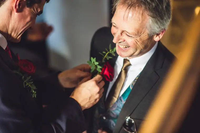 Close-up of a red rose buttonhole being pinned to a laughing man's lapel