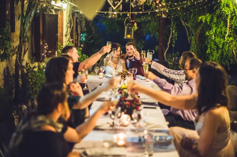 Guests raising glasses in a toast along the long candlelit dinner table