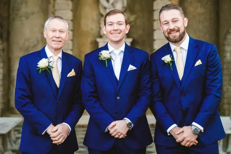 Iain with two groomsmen in matching navy suits smiling at the camera