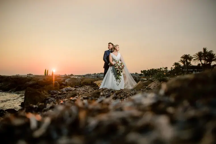 Couple standing on rocks beside the sea as the sun sets, Paphos