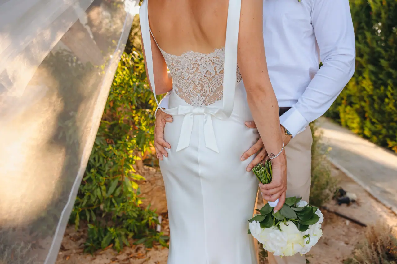 Back of Amy's lace gown with bouquet in hand as Tom stands beside her