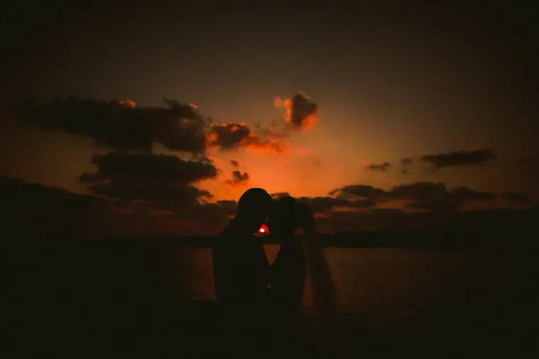 Charlotte and Nathan silhouetted against a deep orange sunset over the sea