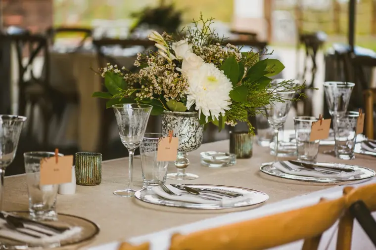 Reception table with white flowers, gold-rimmed plates and glassware under a tent