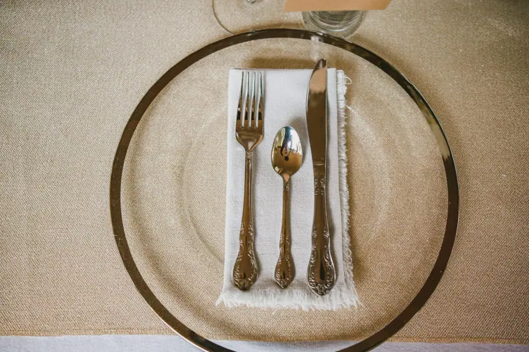 Gold cutlery on a white napkin inside a gold-rimmed charger plate