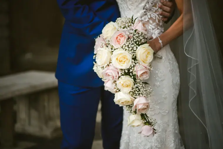 Close-up of the bride's cascading pink and ivory rose bouquet against her lace dress