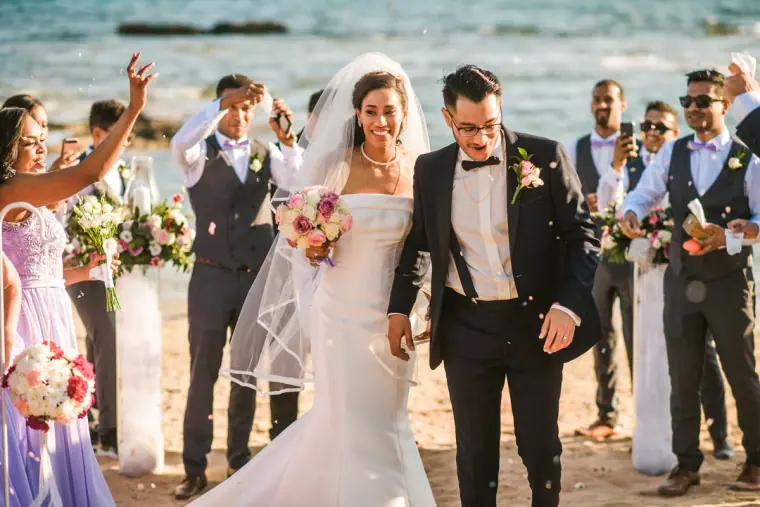 Confetti thrown as the newlyweds walk back up the beach aisle past cheering guests